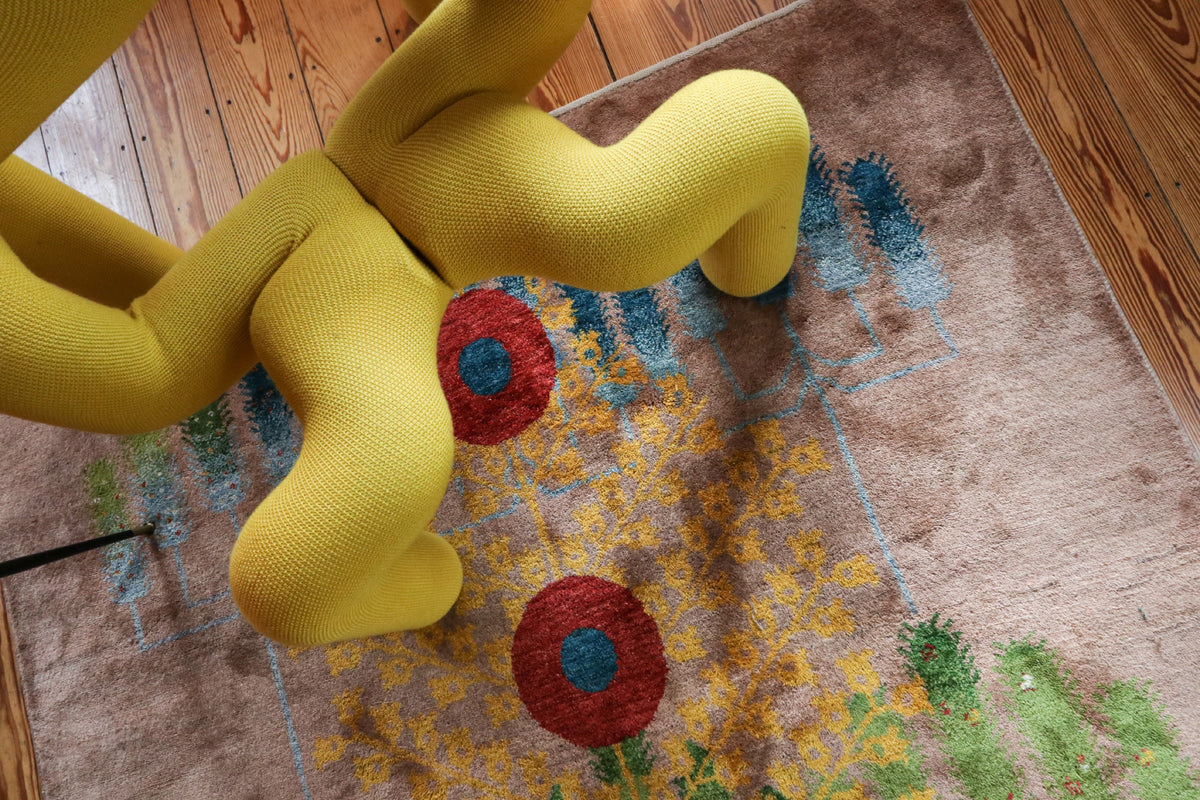 Yellow sculptural chair on a patterned rug over wooden floorboards.