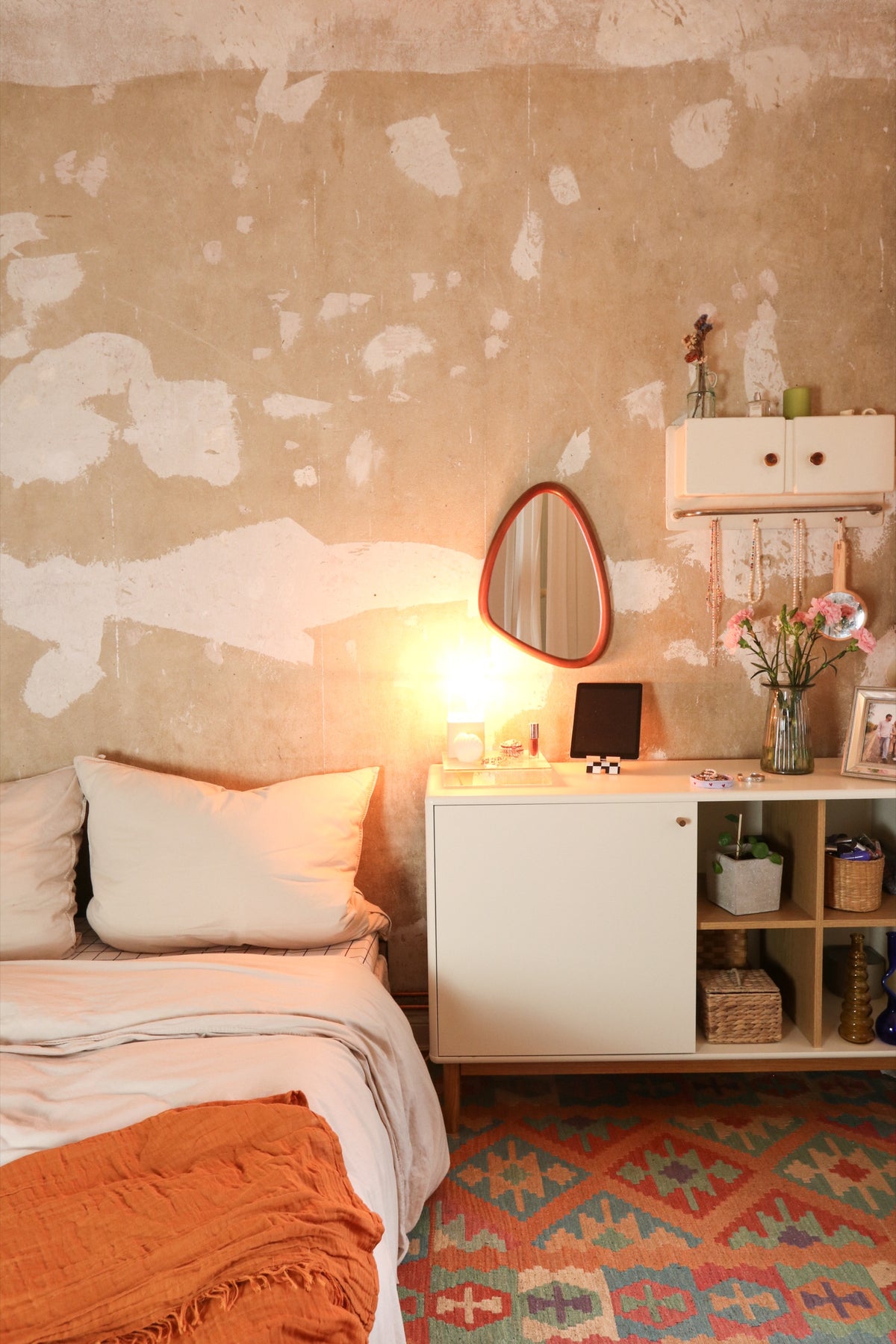 Bedroom with a bed, white sideboard, mirror, and a patterned rug on the floor.