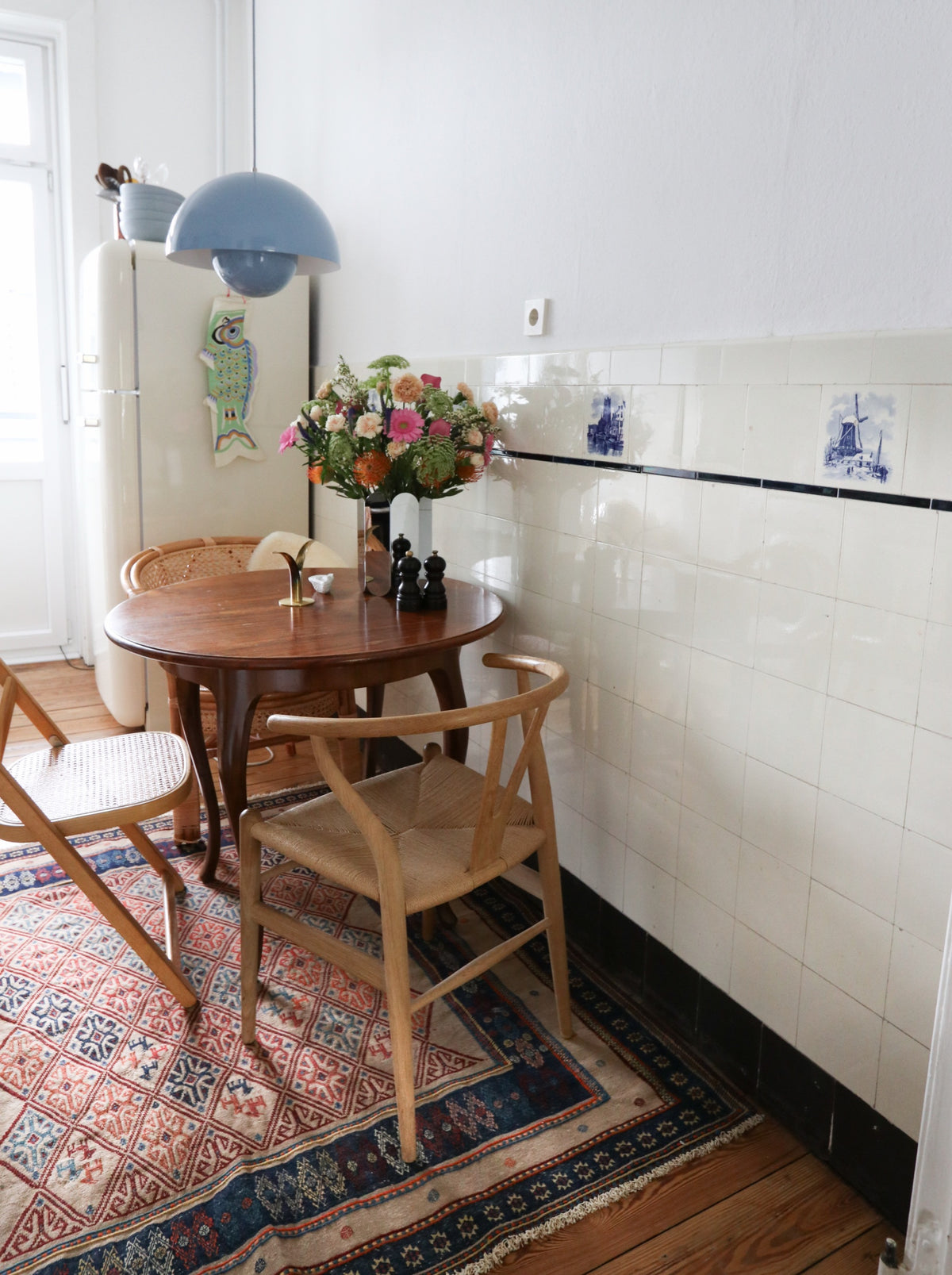 Round wooden table with chairs and a flower bouquet on a patterned rug in the kitchen.