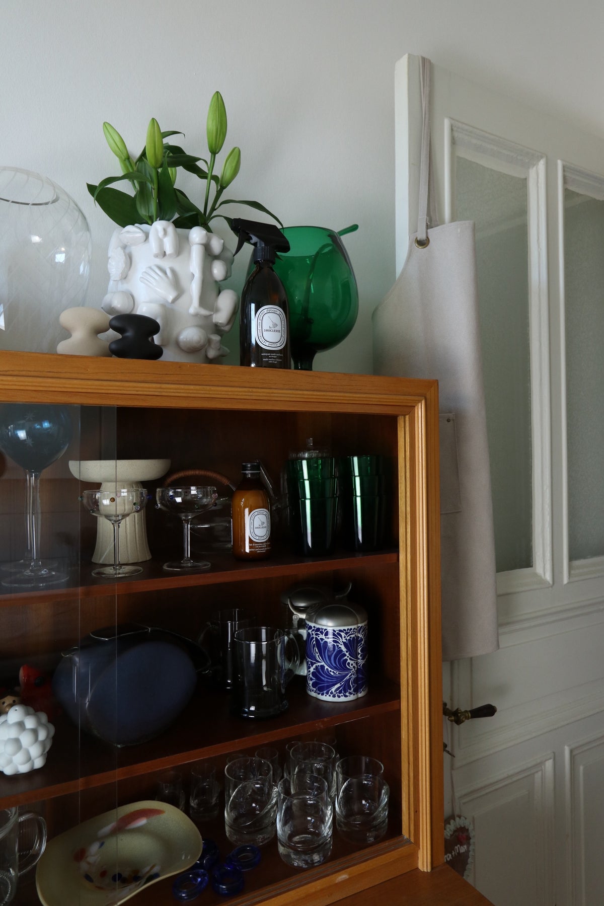 Wooden cabinet with glassware, ceramics, and a vase with buds on top.