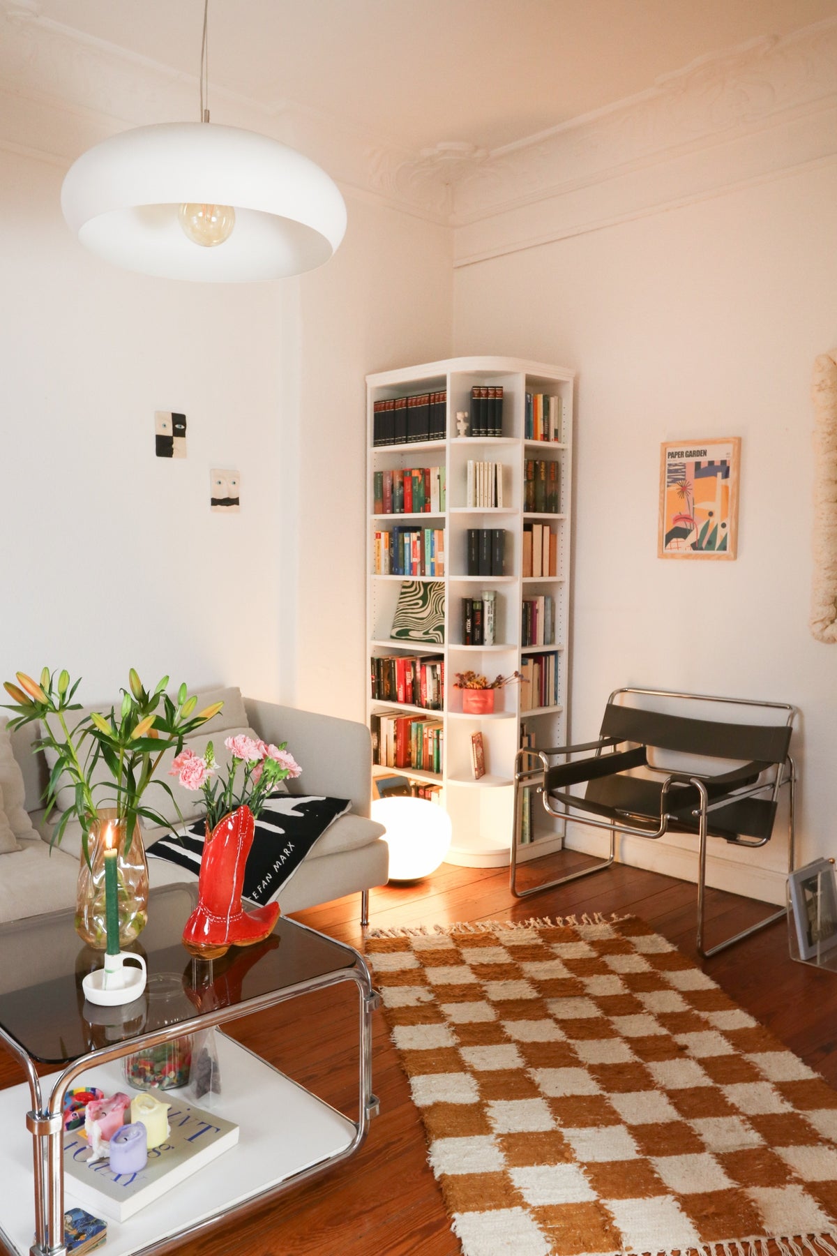 Living room with sofa, armchair, bookshelf, and checkered rug on wooden floor.