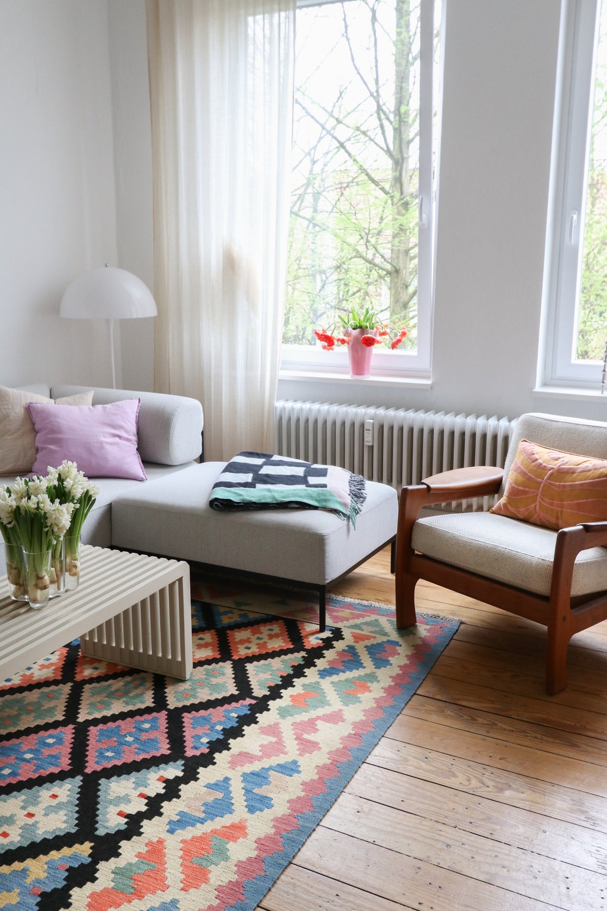 Bright living room with a sofa, armchair, coffee table, and colorful rug on wood floors.