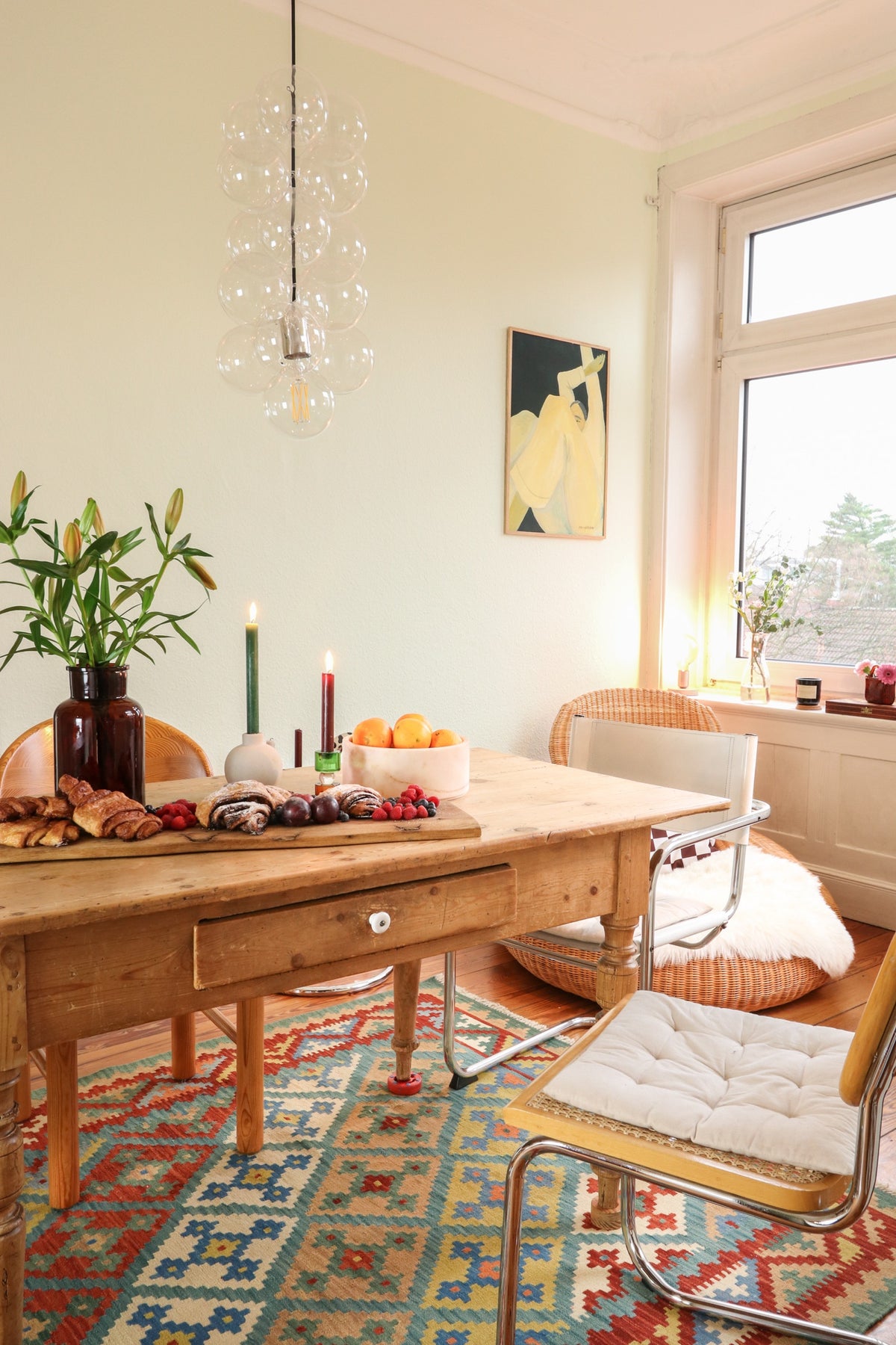 Wooden dining table with chairs and a colorful patterned rug in a bright room.