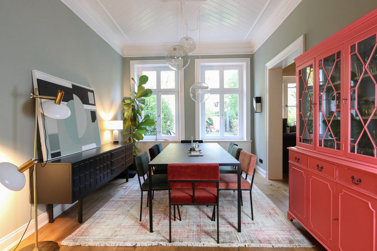 Dining room with a black dining table, colorful chairs, red display cabinet, and fringed rug.
