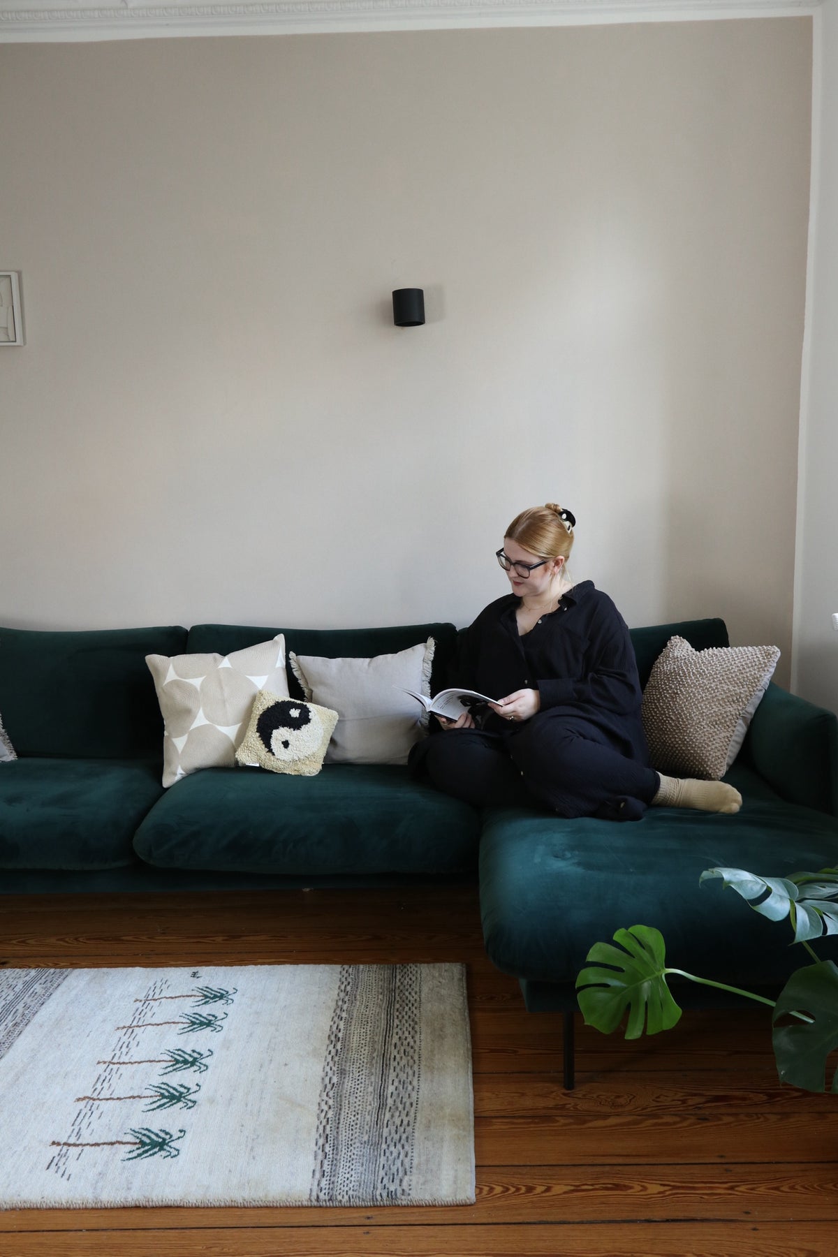 Woman reading on a green sofa, with a light patterned rug on a wooden floor in front.