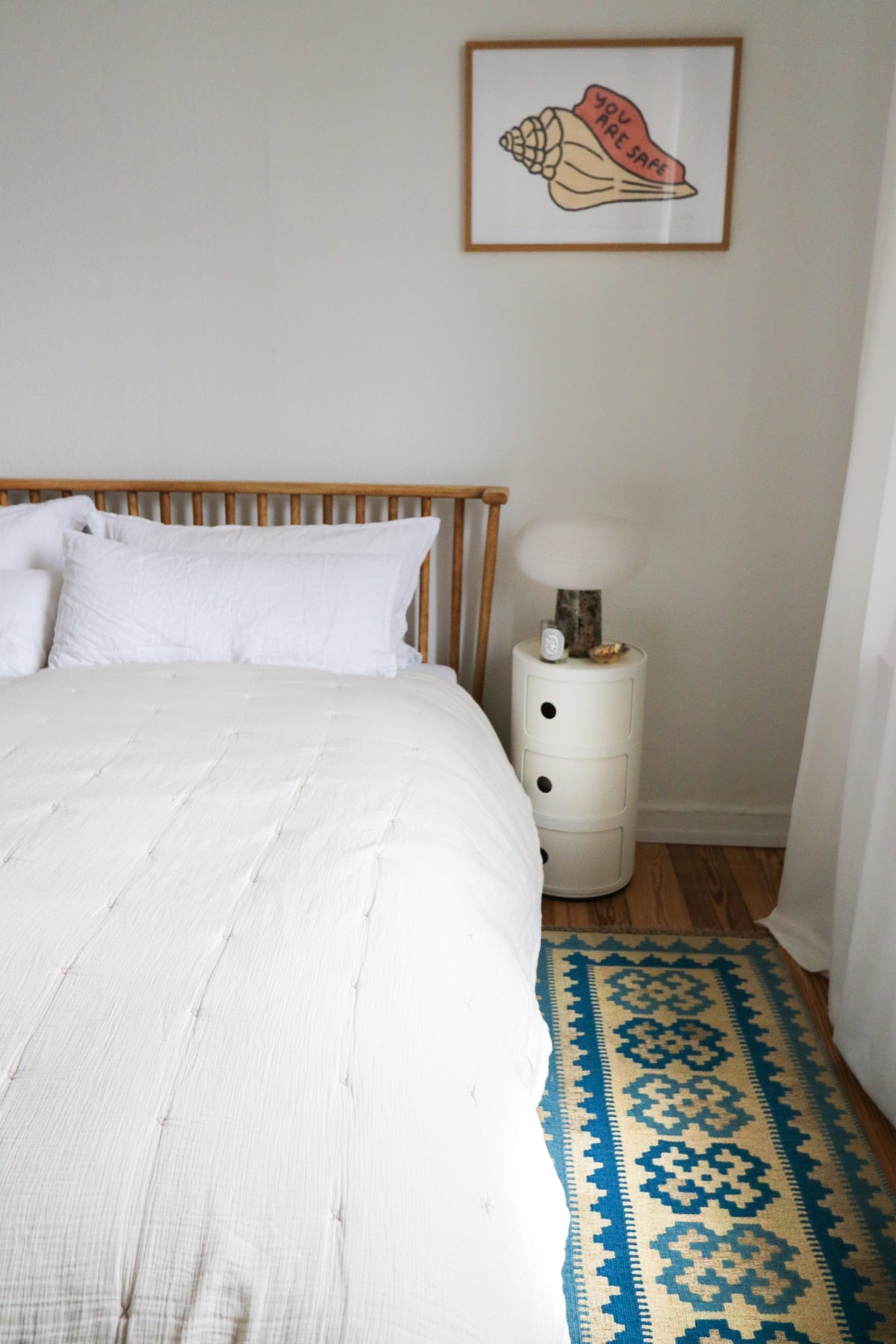 Bed with white bedding, round bedside table, and blue and yellow rug in a bedroom.