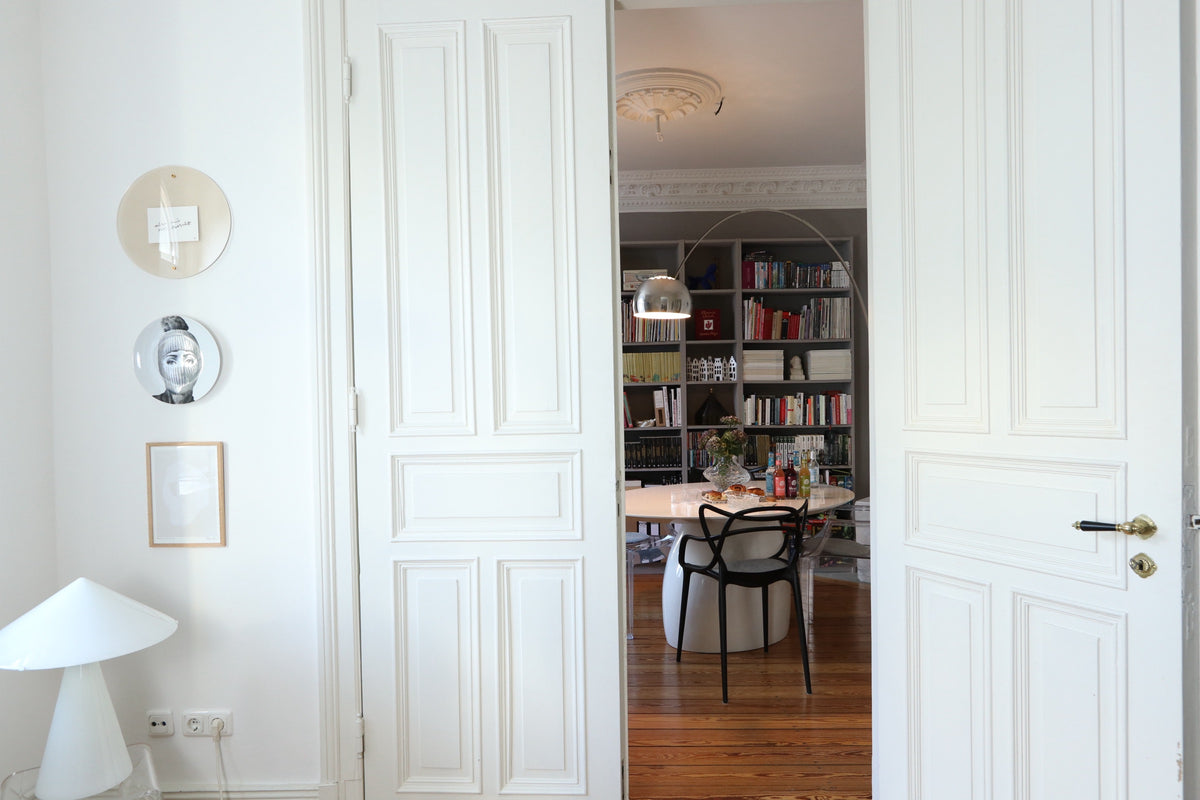 View through white double doors to a dining table and a bookcase with a floor lamp.